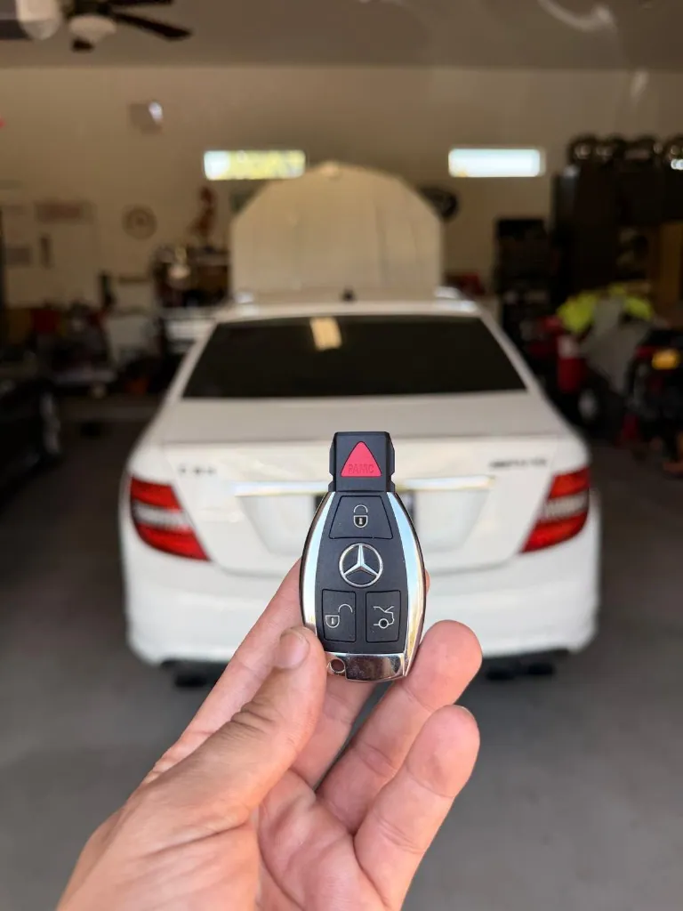 Mercedes-Benz remote key shown with the customer's white sedan after an all-keys-lost job